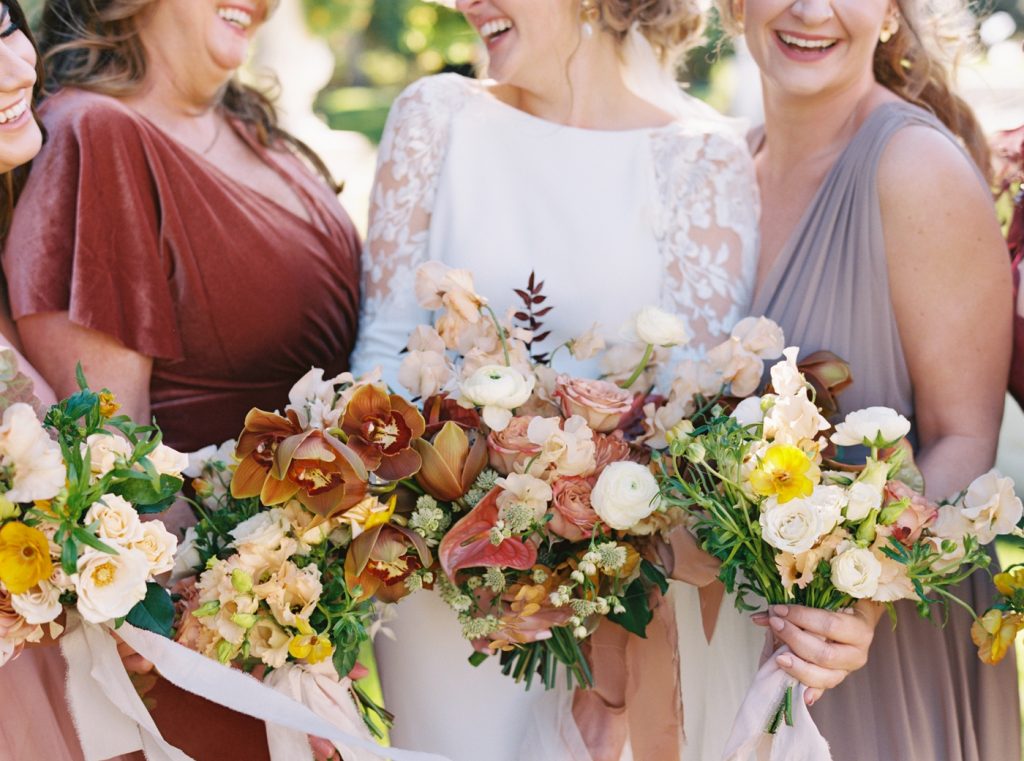 Bridal bouquet by Gray Harper with copper cymbidium orchids, cream ranunculus, mauve roses, and handpicked flowers in shades of honey and blush.
