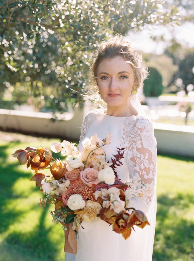 Bridal bouquet by Gray Harper with copper cymbidium orchids, cream ranunculus, mauve roses, and handpicked flowers in shades of honey and blush.
