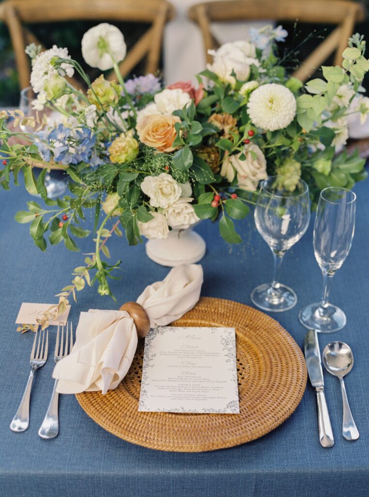 Blue wedding table setting with rattan charger and pastel wedding flowers