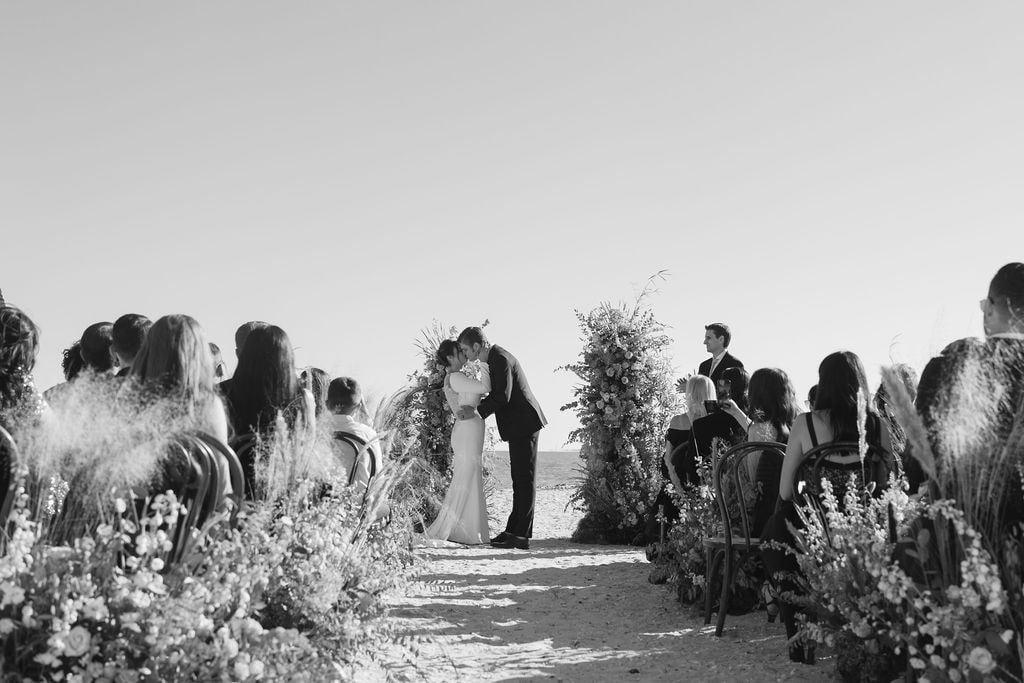 Black and white photo of couple kissing at beach wedding ceremony