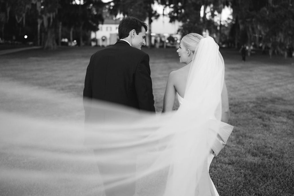 Black and white photo of bride and groom with wedding veil blowing