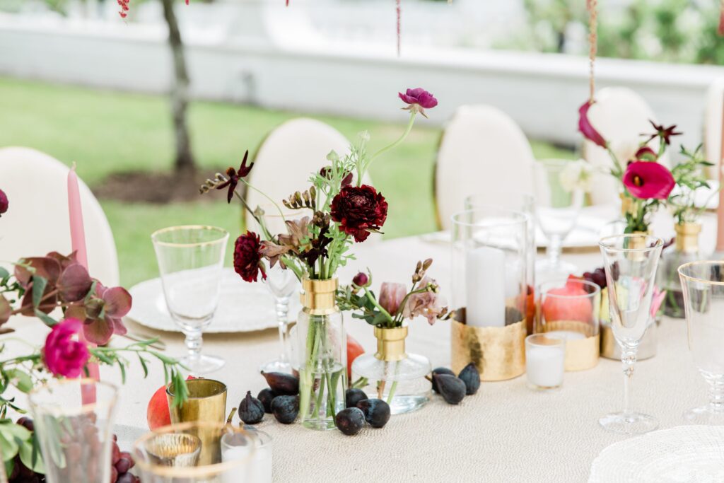 Bud vases with burgundy flowers and fruit on table