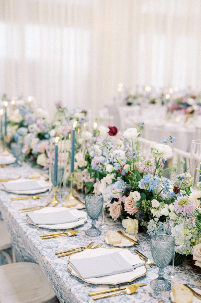 Blue and white wedding table with blue water goblets, gold cutlery and lush floral runner