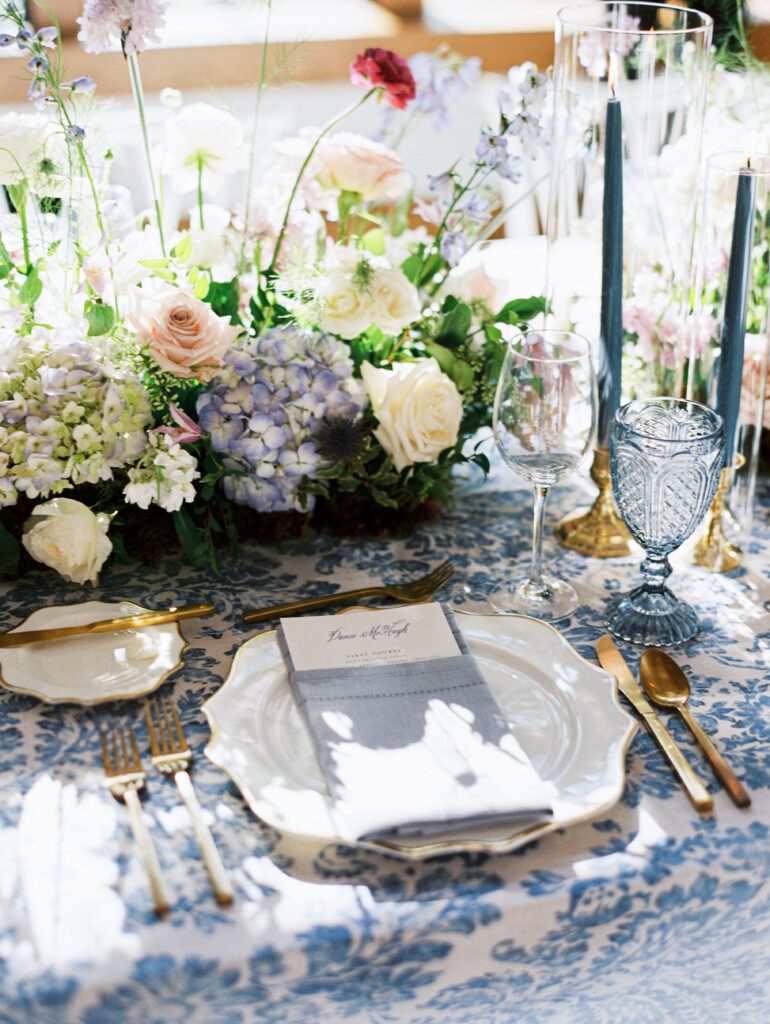 Blue and white linen with gold charger plate, gold cutlery, blue napkins and blue water goblets