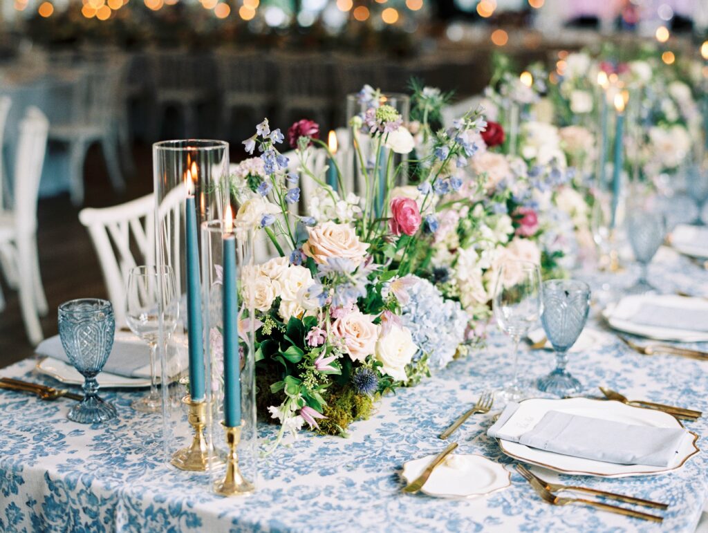Blue and white linen with gold charger plate, gold cutlery, blue water goblets and floral runner