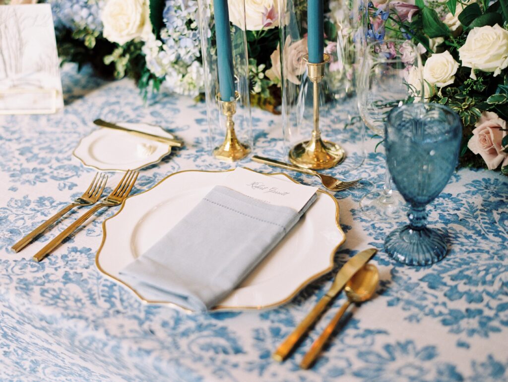 Wedding table with blue and white pattern linen with gold charger plate, gold cutlery and blue water goblet
