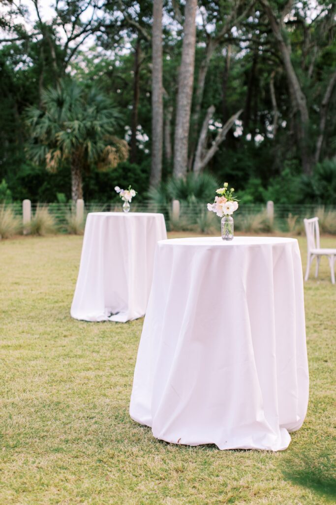 White cocktail tables with simple flower arrangements outside